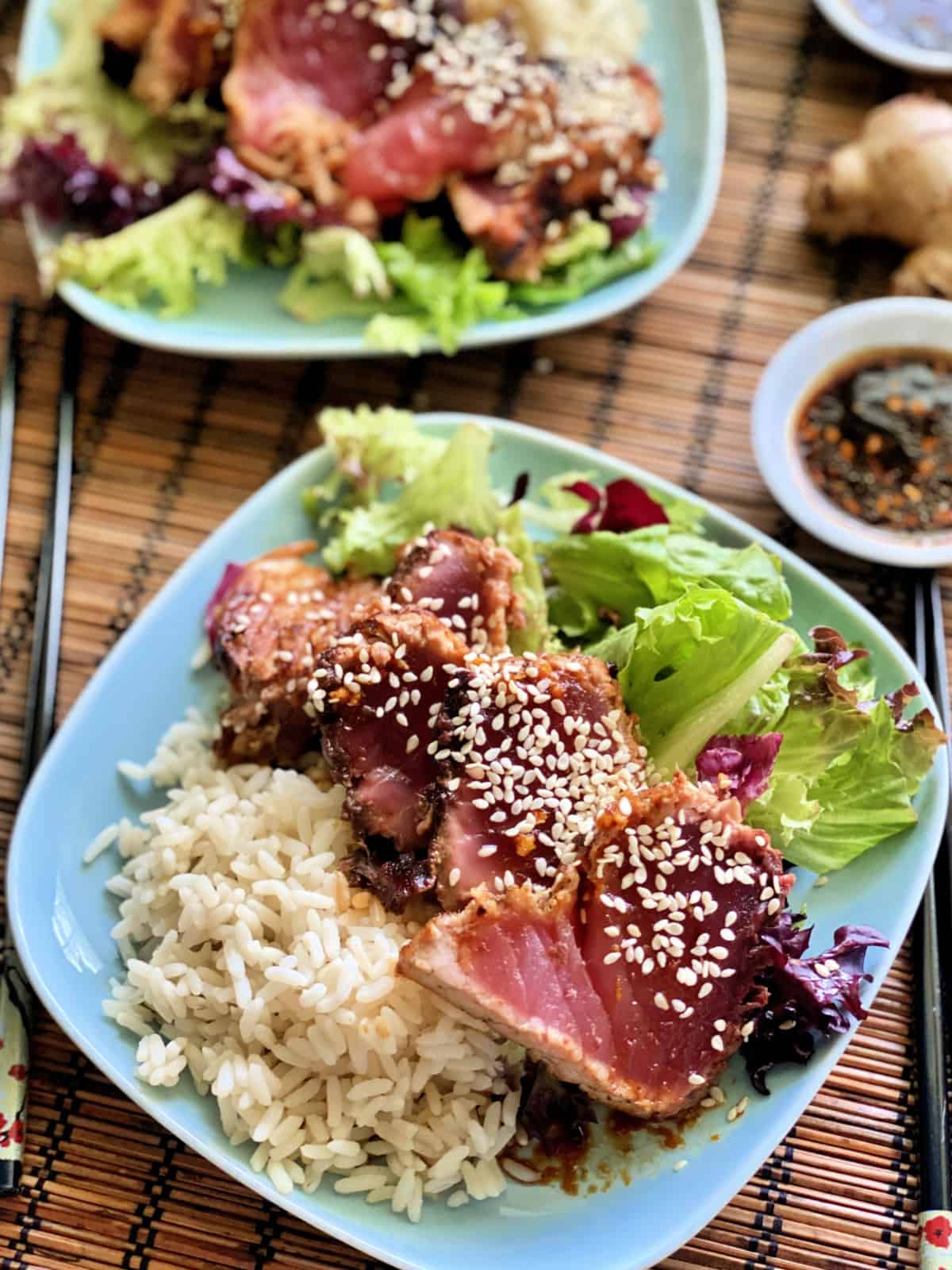 Top view of a blue plate with white rice and salad on it with seared sliced tuna on top.