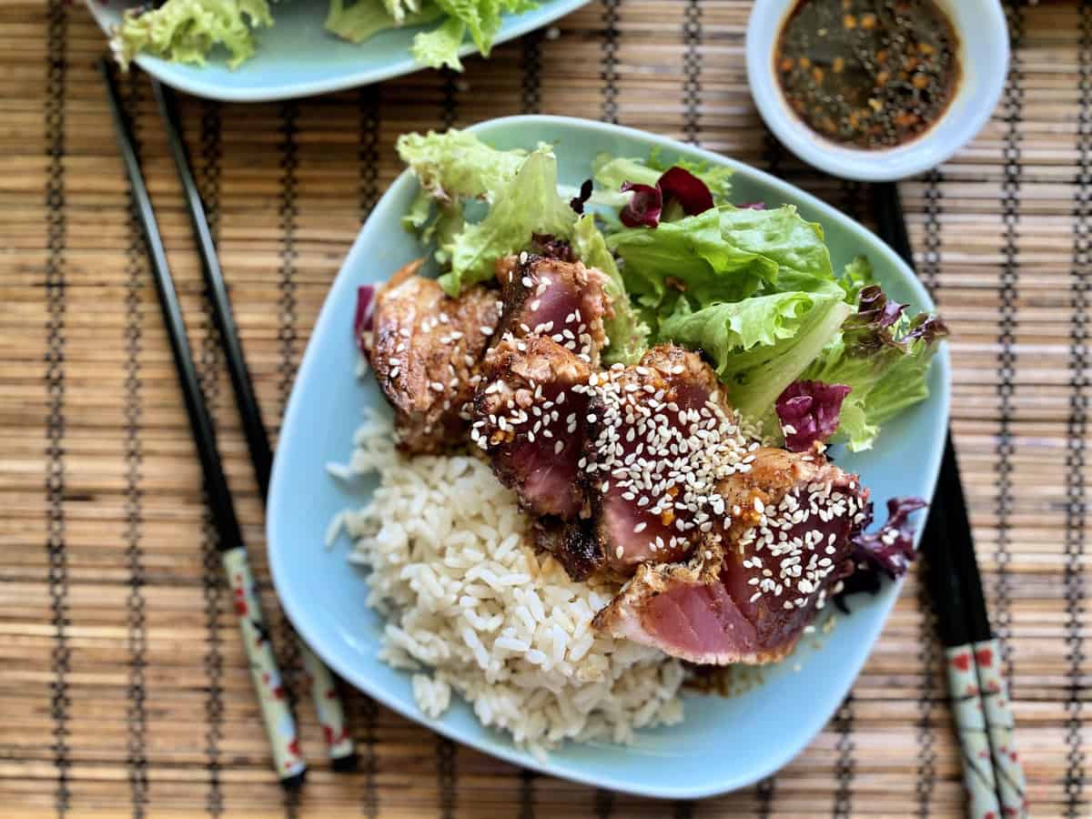 Top view of seared tuna with sesame seeds on top of salad and  rice.