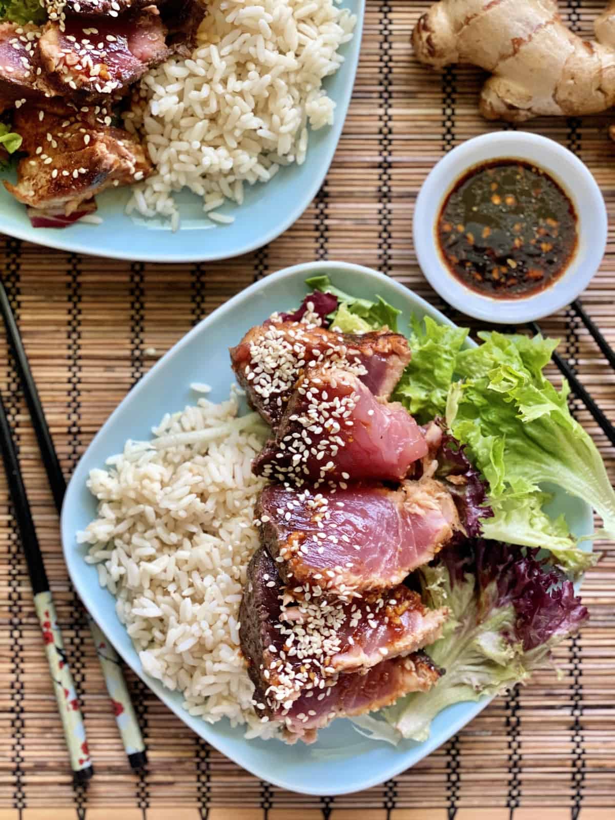 Top view of seared tuna on a blue plate with rice and salad with sauce on the side.