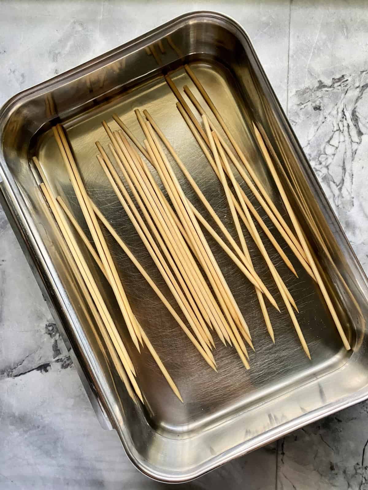 Wood skewers in a metal tray soaking in water. 