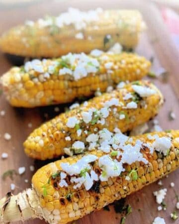 Picture of 4 grilled corn on the cob topped with fetta cheese.
