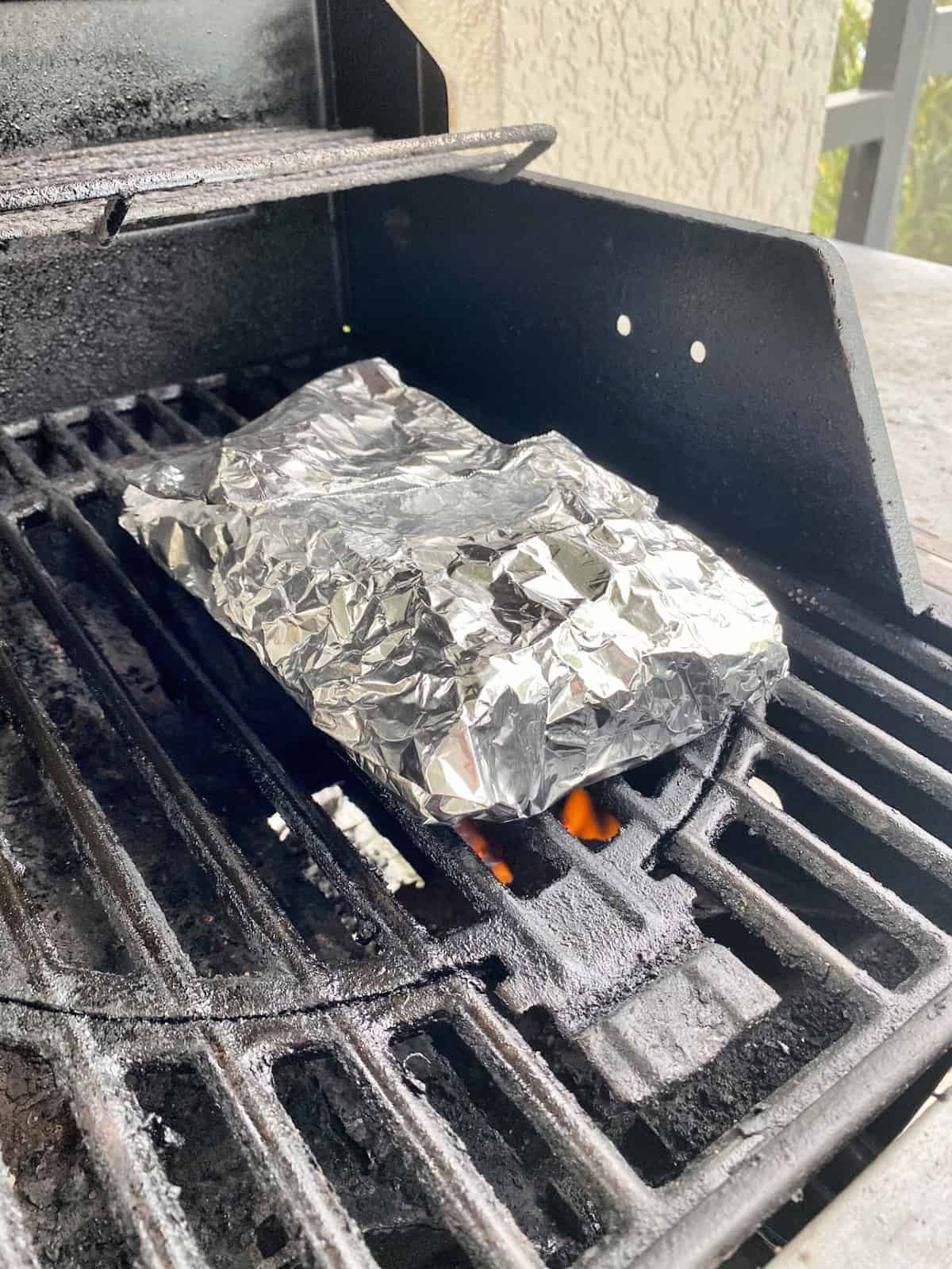 Aluminum foil pouch on a hot gas grill with flames underneath it.