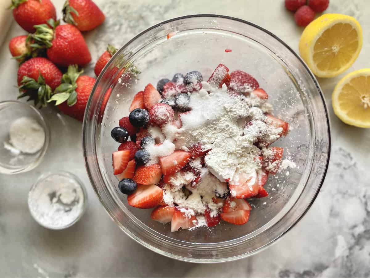 Top view of bowl with berries, cornstarch, and sugar on marble countertop. 