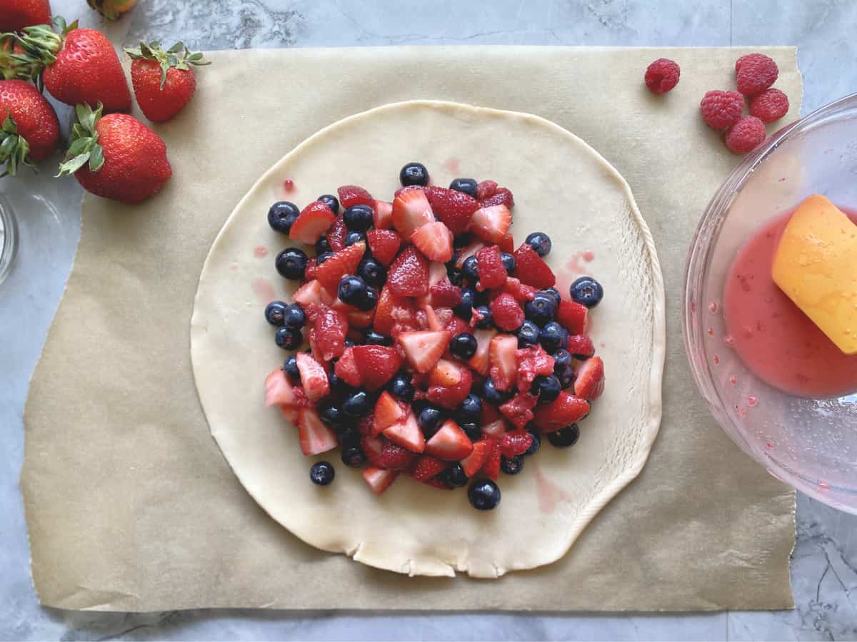 Top view of berries in the center of a pie crust on brown parchment paper. 