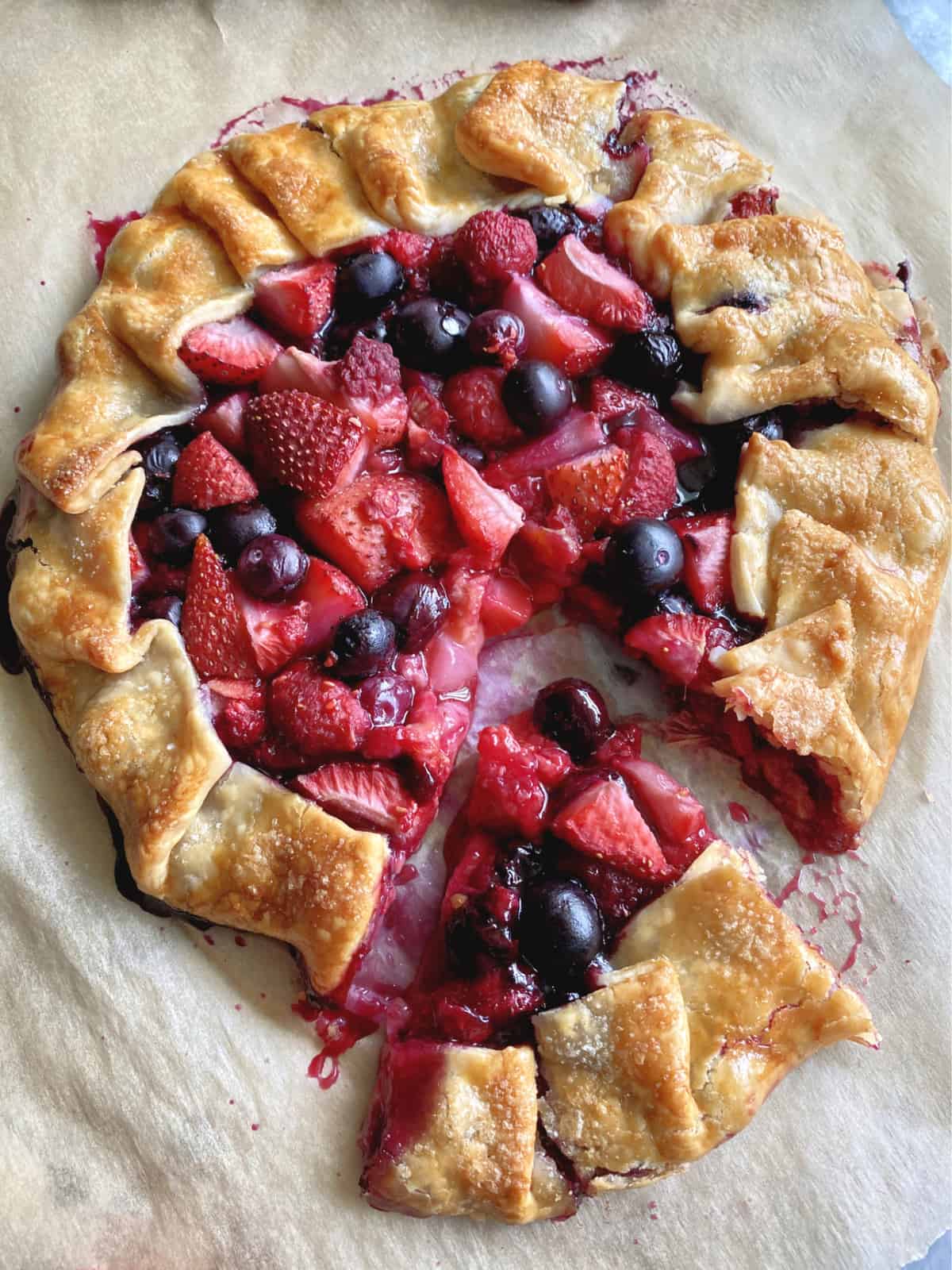 Top view of sliced open faced pie with berries and a slice cut out of it. 