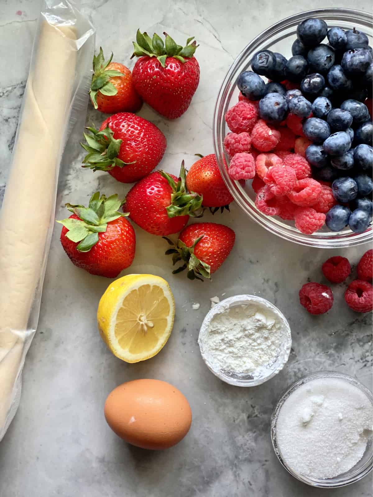Pie crust dough, strawberries, blueberries, raspberries, lemon, egg, sugar and cornstarch.