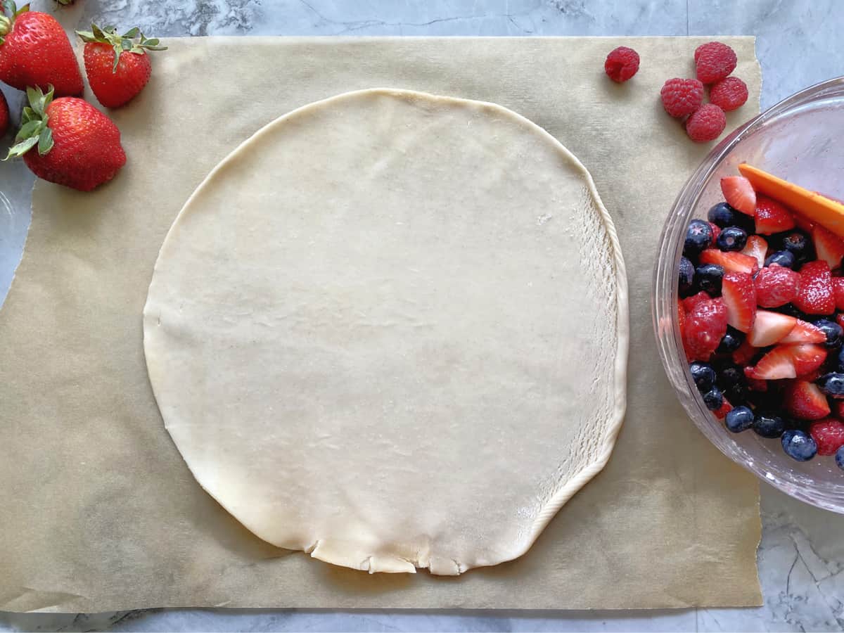 Pie dough rolled out on parchment paper with berries in bowl next to it. 