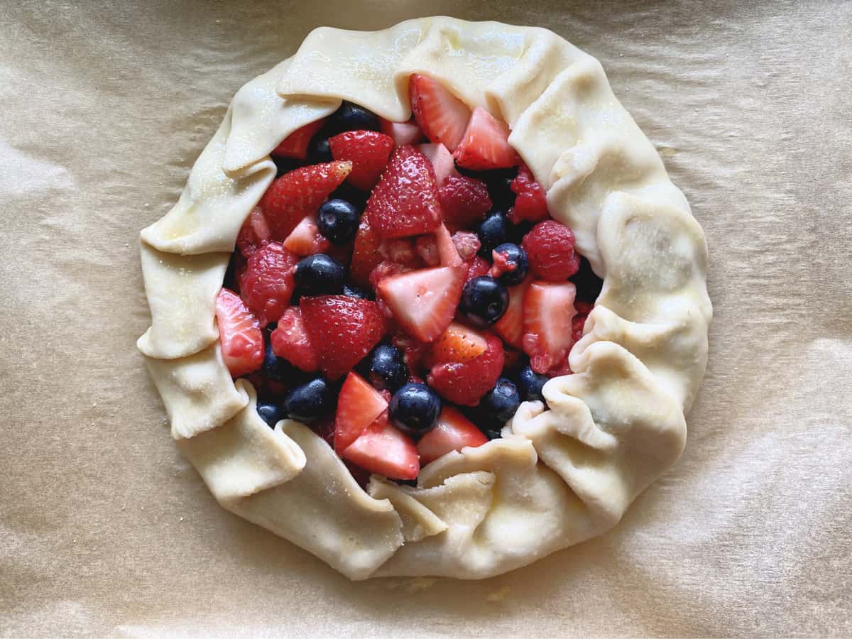 Top view of folded pie crust with berries on brown parchment paper. 