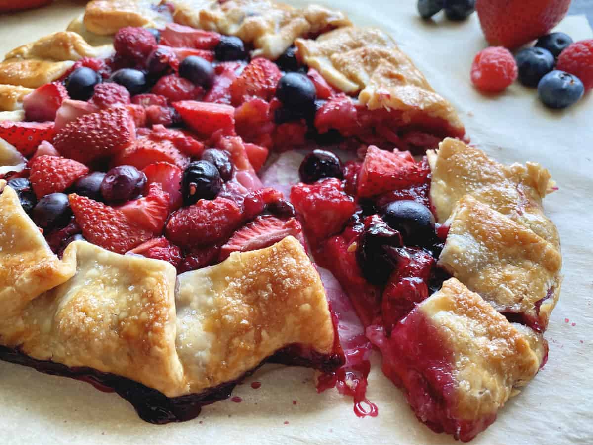 Cooked open faced pie with slice cut of strawberries, blueberries, and raspberries. 