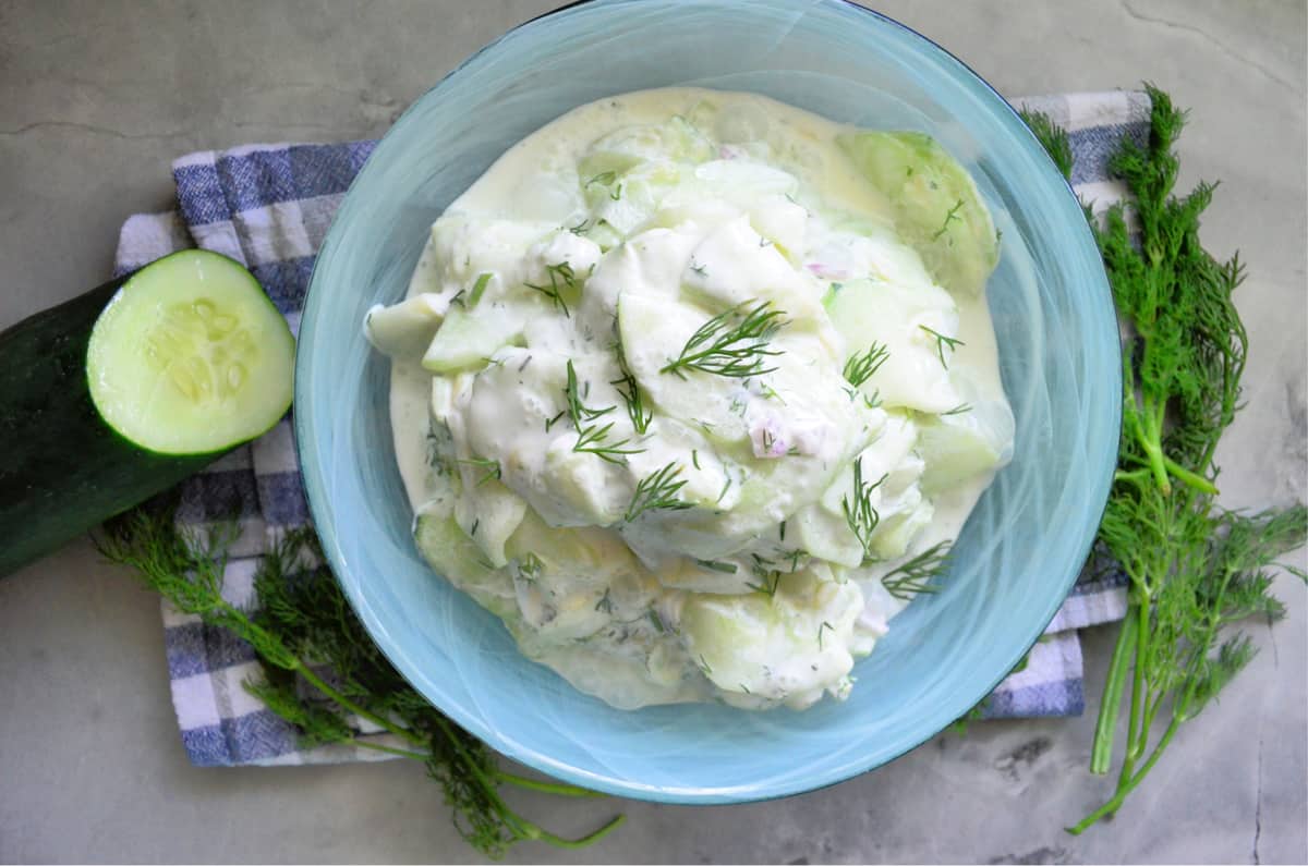 Top view of thinly sliced cucumbers in a white sauce with fresh dill and red onion.