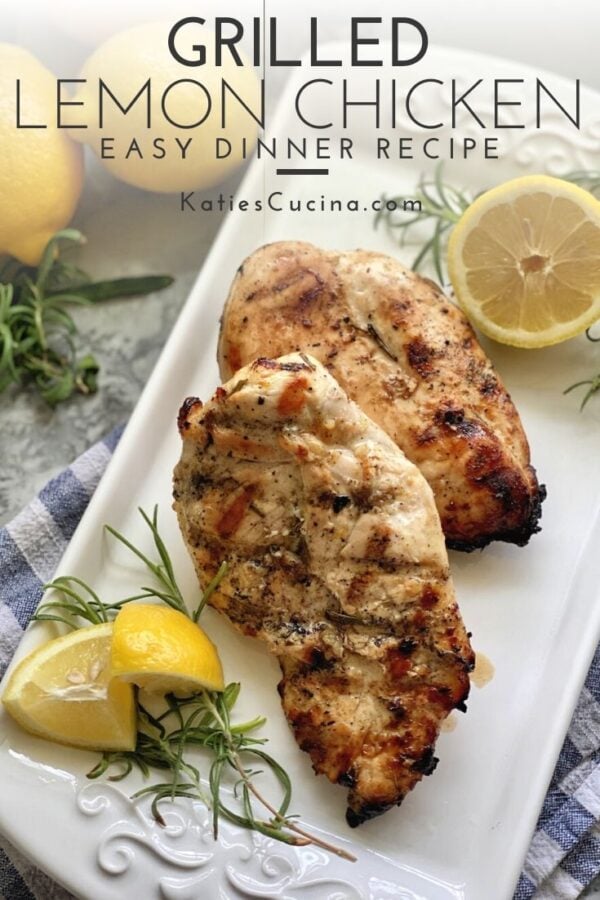 Grilled chicken breast on a white platter with fresh lemon wedges and rosemary.