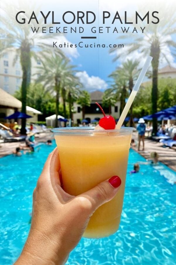 Womens hand with red nail polish holding tropical drink poolside.