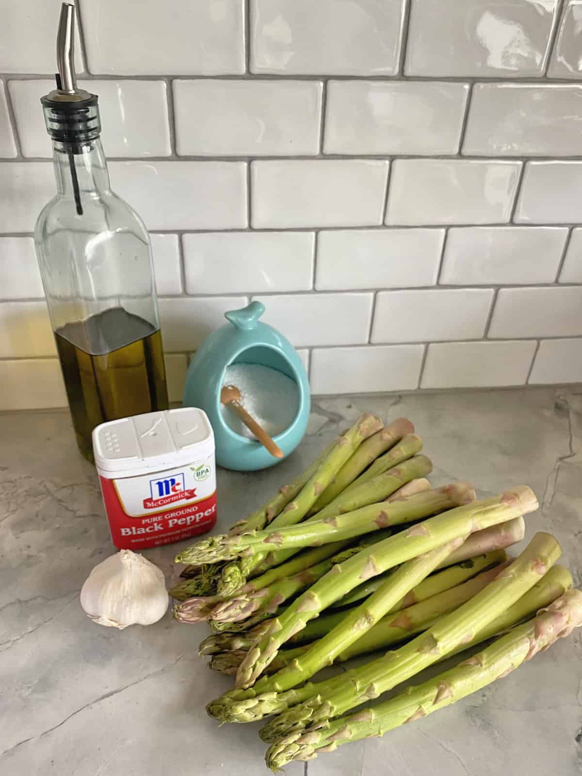 Ingredients: Olive oil, salt, pepper, garlic, and asparagus on marble countertop.