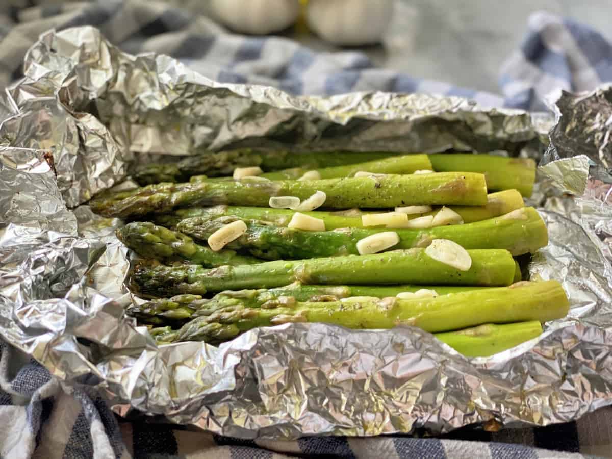 Side view of cooked asparagus with sliced garlic on top in aluminum foil.