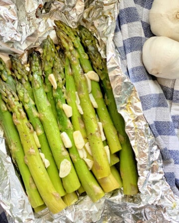 Asparagus with garlic in aluminum foil pouch on a blue and white checkered towel.