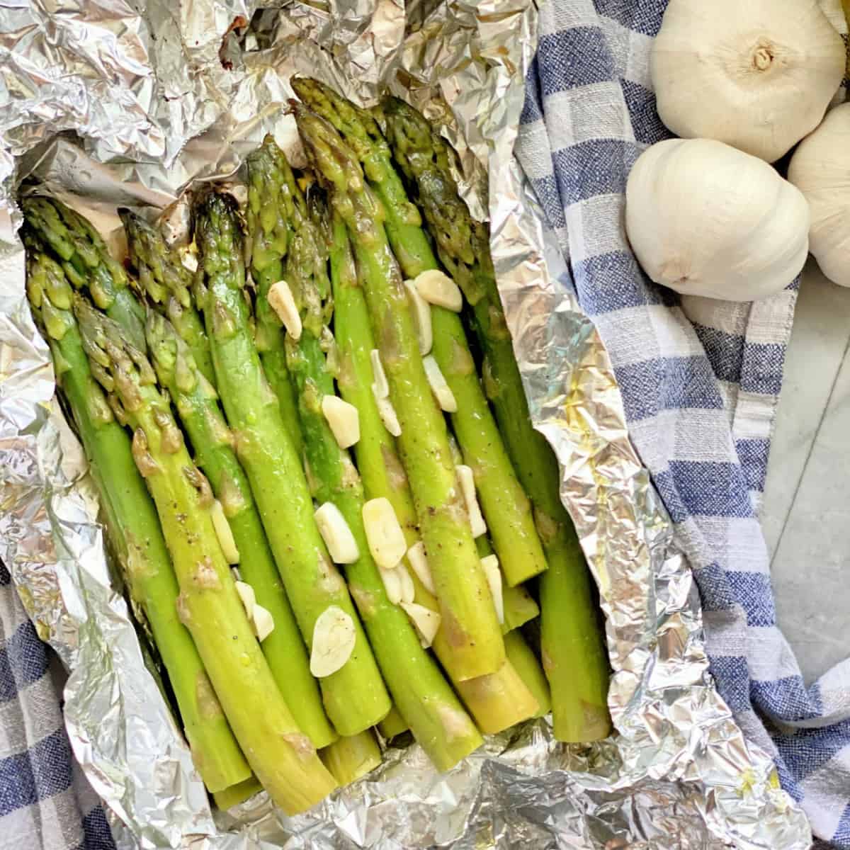 Asparagus with garlic in aluminum foil pouch on a blue and white checkered towel.