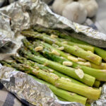 silver foil with green asparagus with garlic slices inside