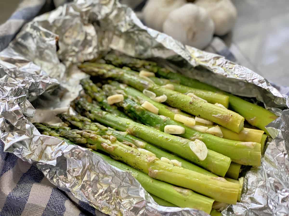 Side view of a foil pouch with cooked asparagus and sliced garlic.