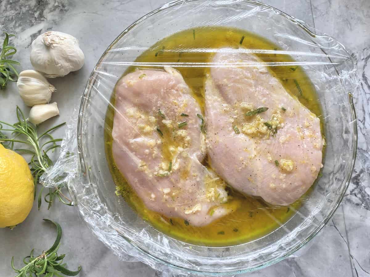 Top view of raw chicken in a marinade covered with plastic wrap.
