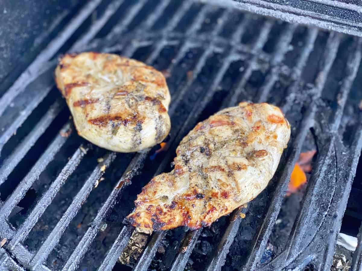 Chicken breast on a grill with flames underneath the grate.