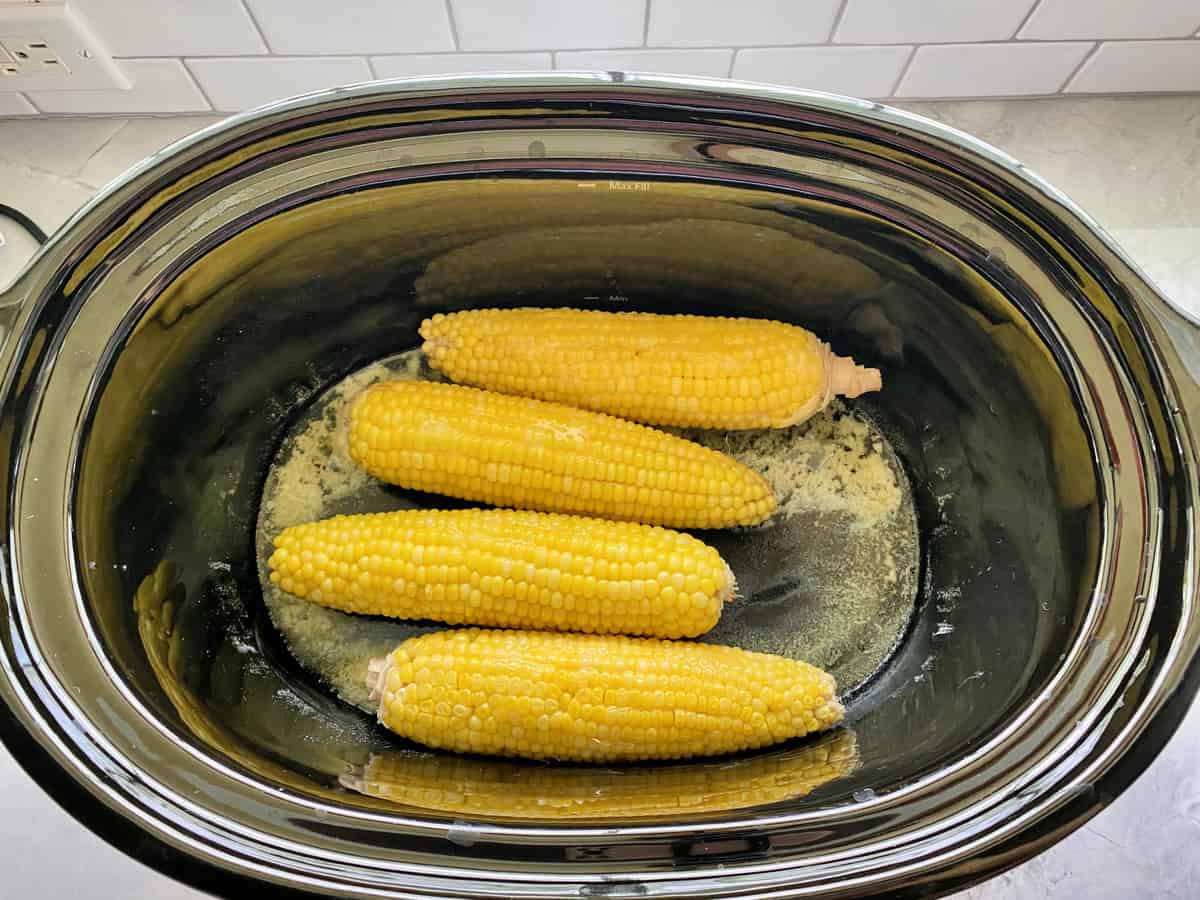 Top view of cooked corn on the cob sitting in melted butter in a slow cooker.