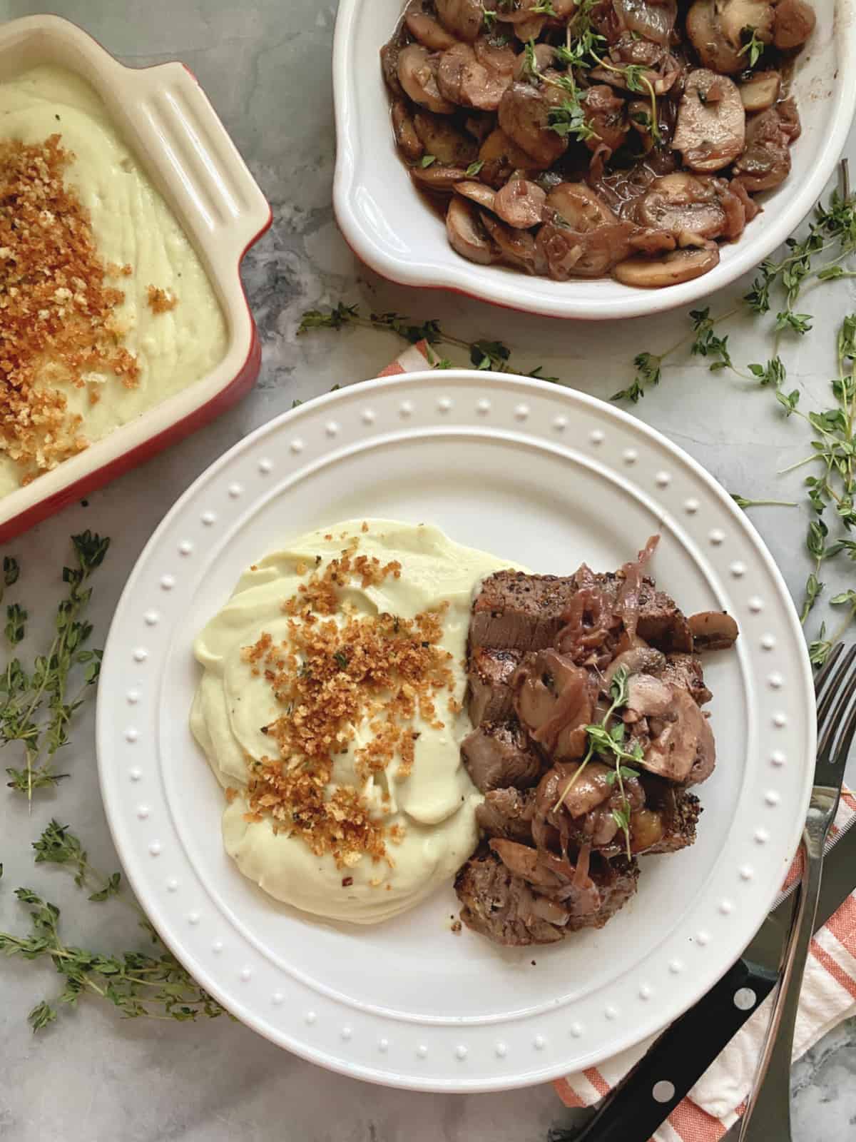 Top view of steak dinner plated with bowl of sauteed mushrooms and potatoes.