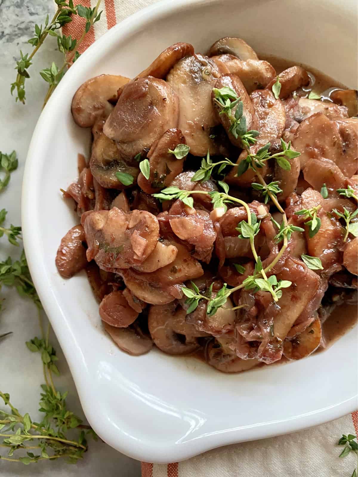 Close up of sauteed mushrooms in wine sauce with fresh sprigs of thyme on top and around the bowl.