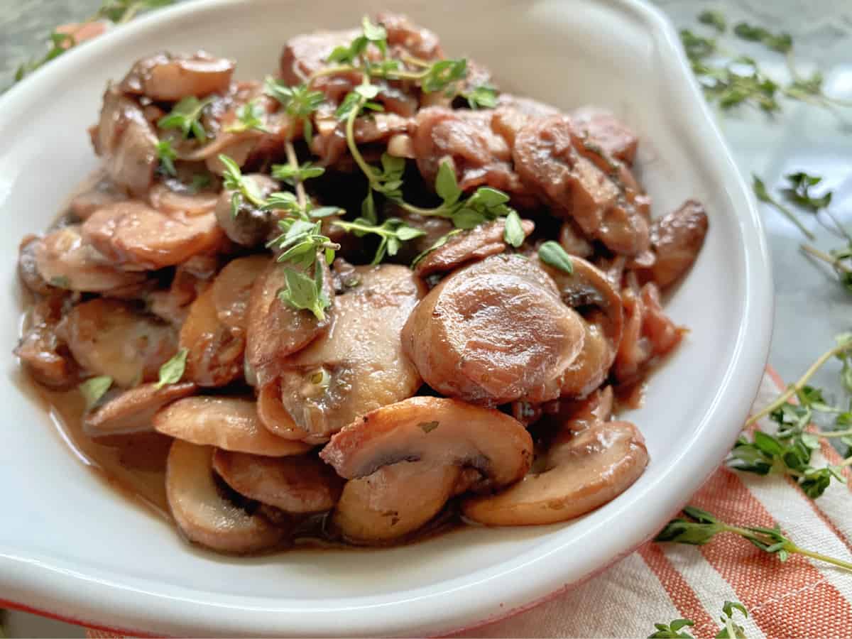 Up close of a white dish with sauteed mushrooms with fresh sprigs of thyme on top. 
