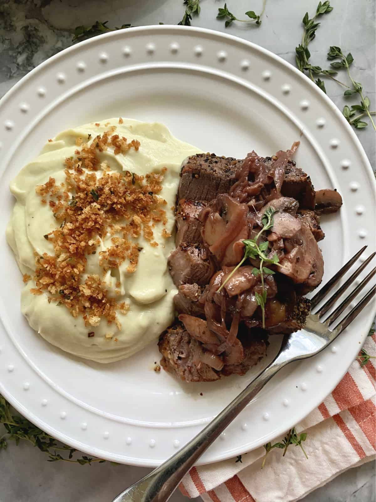 Top view of white plate with potatoes and steak with mushrooms sauce on top.