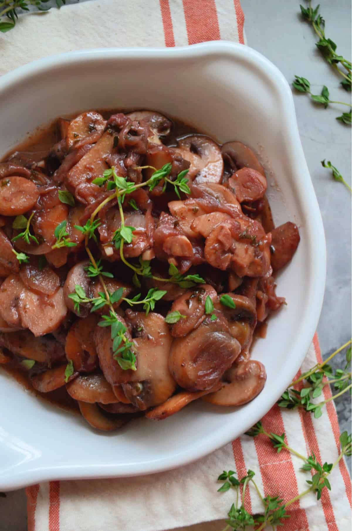 Top view of white bowl with sauteed mushrooms and onions with fresh thyme sprigs on top.