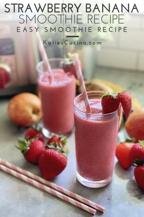 Two glass cups with pink smoothies in it with straws and fruit on counter.