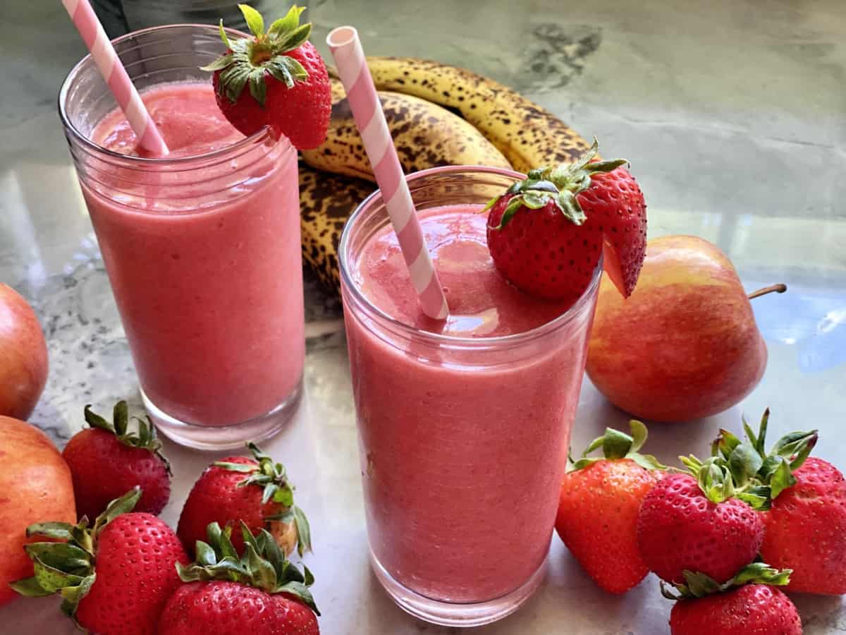 Glass filled with a strawberry smoothie with strawberries on the counter.