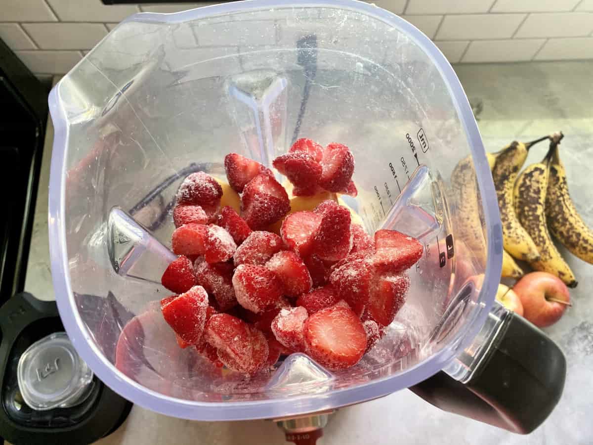 Top view of a blender with frozen strawberries in it.