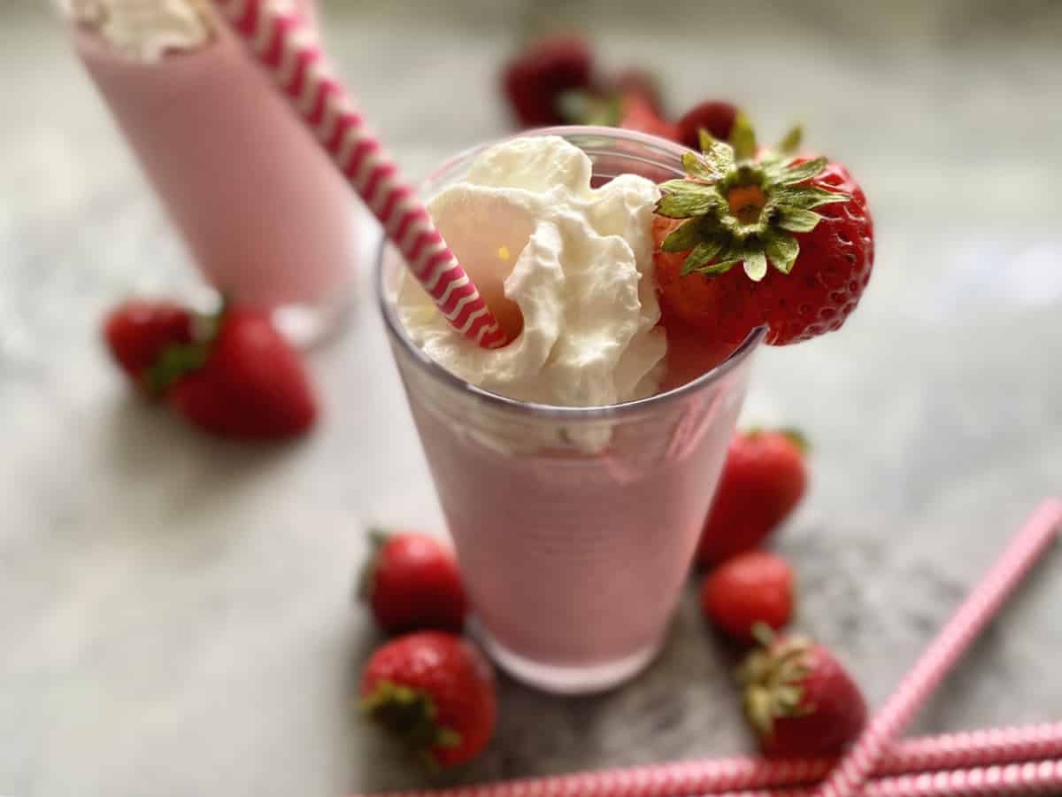 Two glasses of strawberry milkshake with whipped cream on a marble countertop.