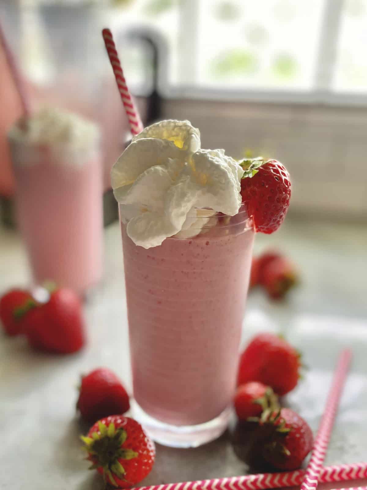Pink milkshake in a glass with whipped cream and fresh strawberries with pink straw. 
