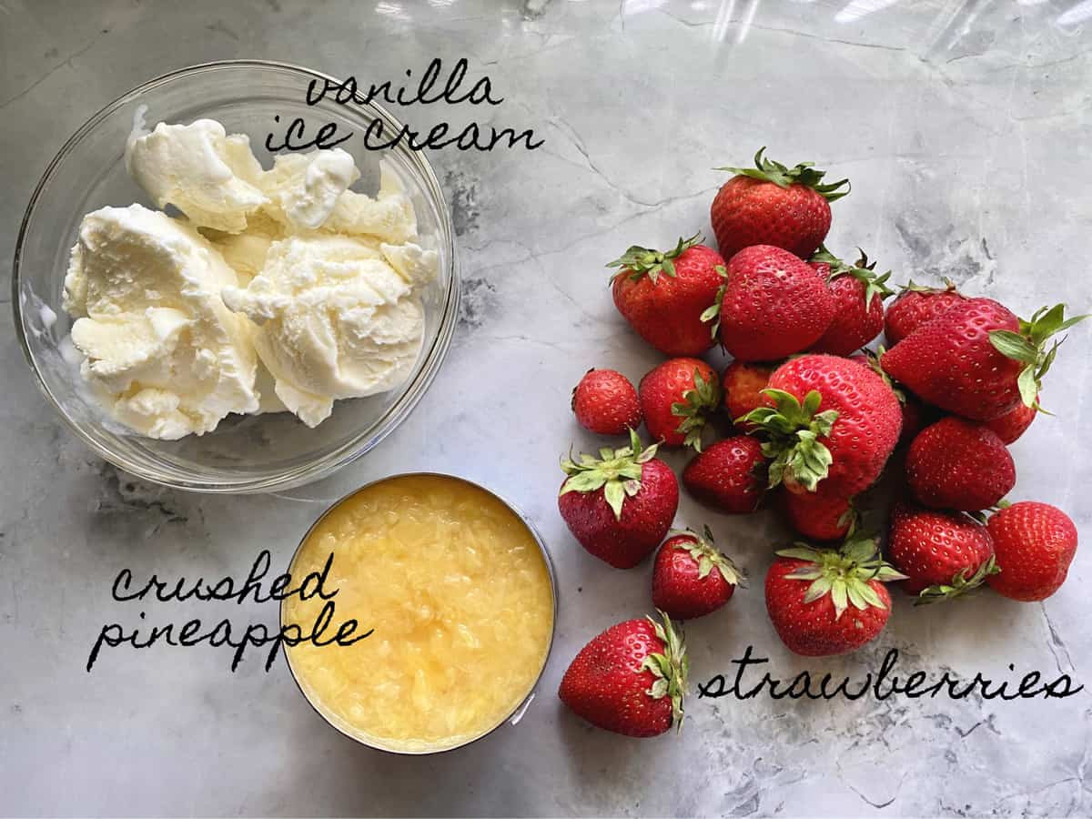 Ingredients on a marble countertop: vanilla ice cream, crushed pineapple, and strawberries.