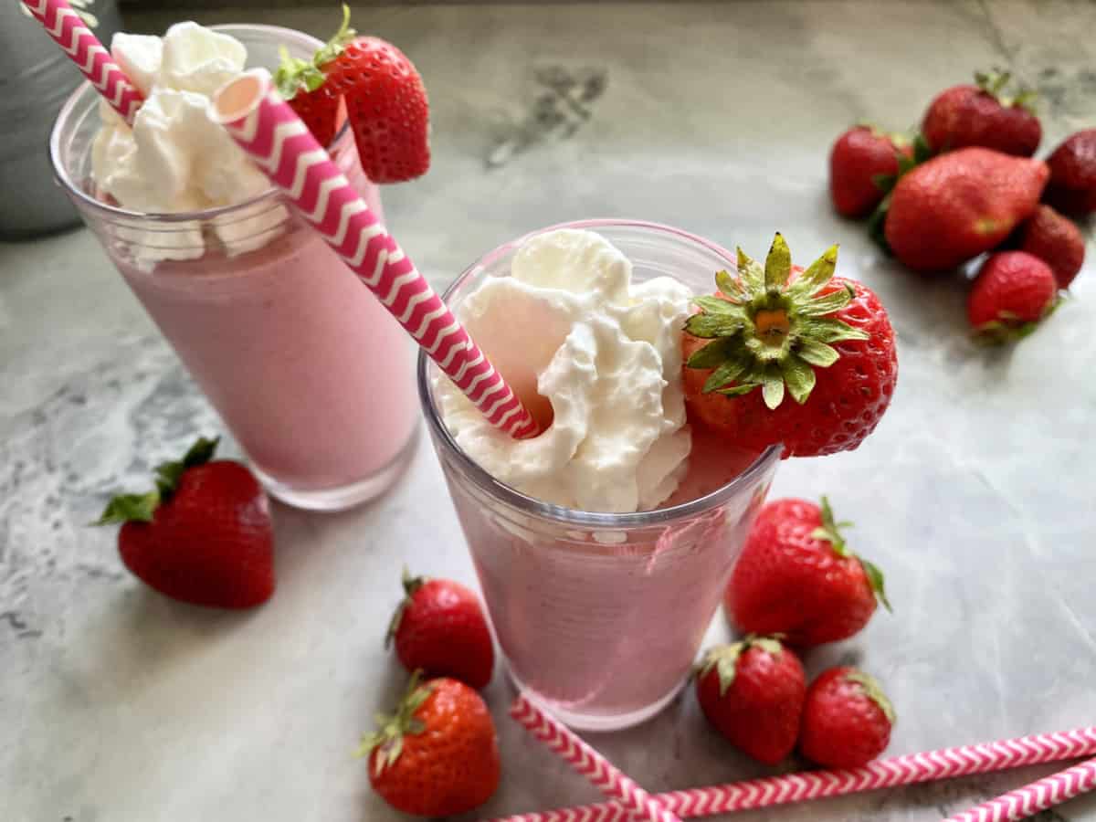 Top view of strawberry milkshake with whipped cream and fresh strawberry and pink and white straw. 