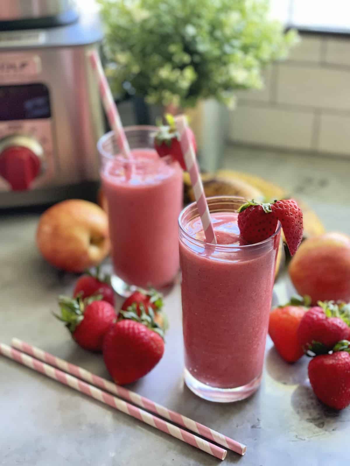 Stawberry smoothie in a glass with fresh strawberries and paper straws around glass.