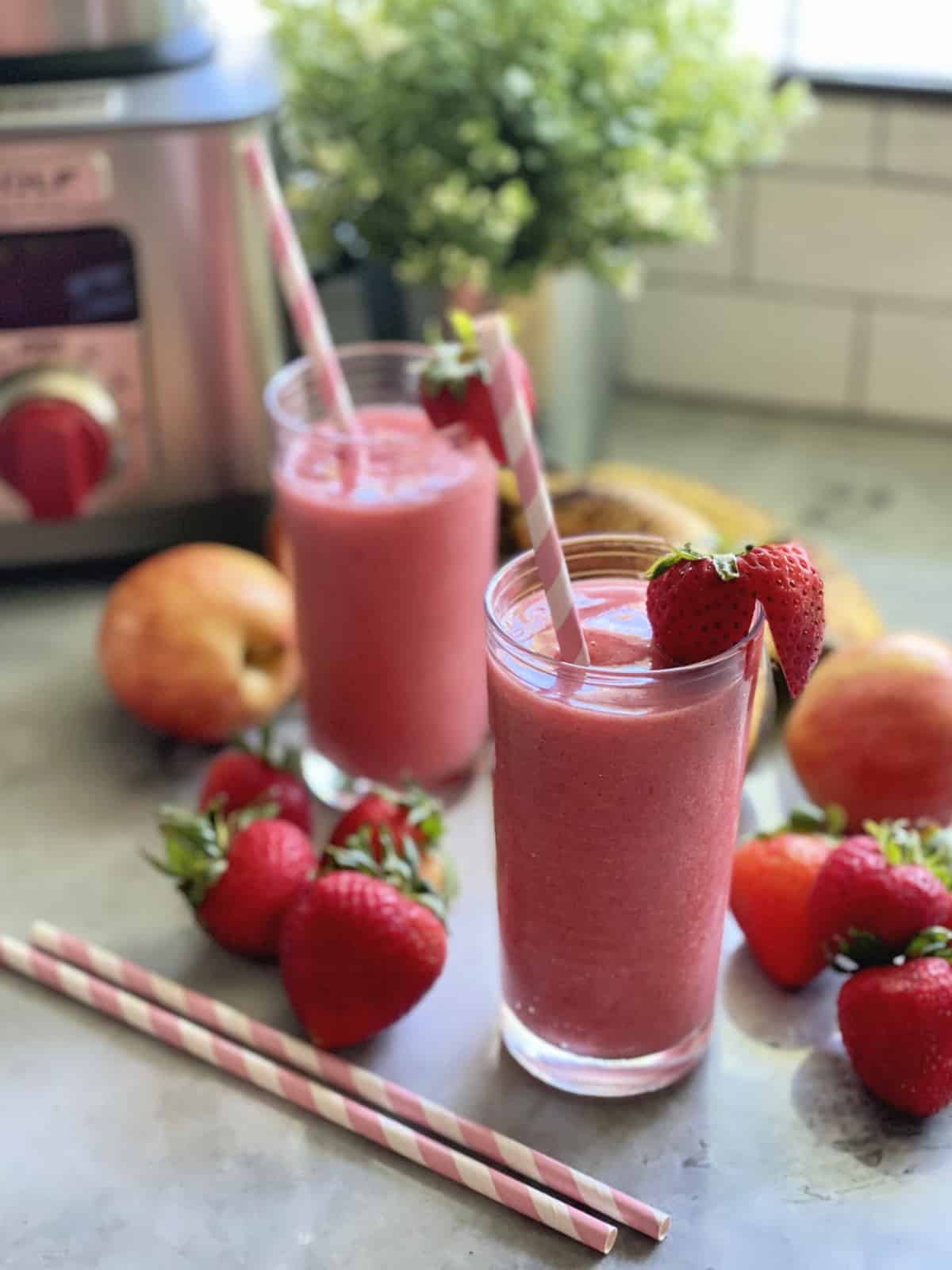 Stawberry smoothie in a glass with fresh strawberries  and paper straws around glass.