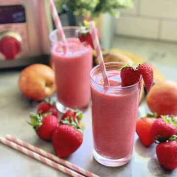 Two glasses filled with a pink smoothie with strawberries and paper straws in the glasses.