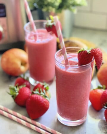 Two glasses filled with a pink smoothie with strawberries and paper straws in the glasses.