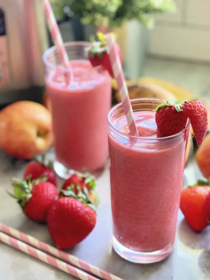 Two glasses filled with a pink smoothie with strawberries and paper straws in the glasses.