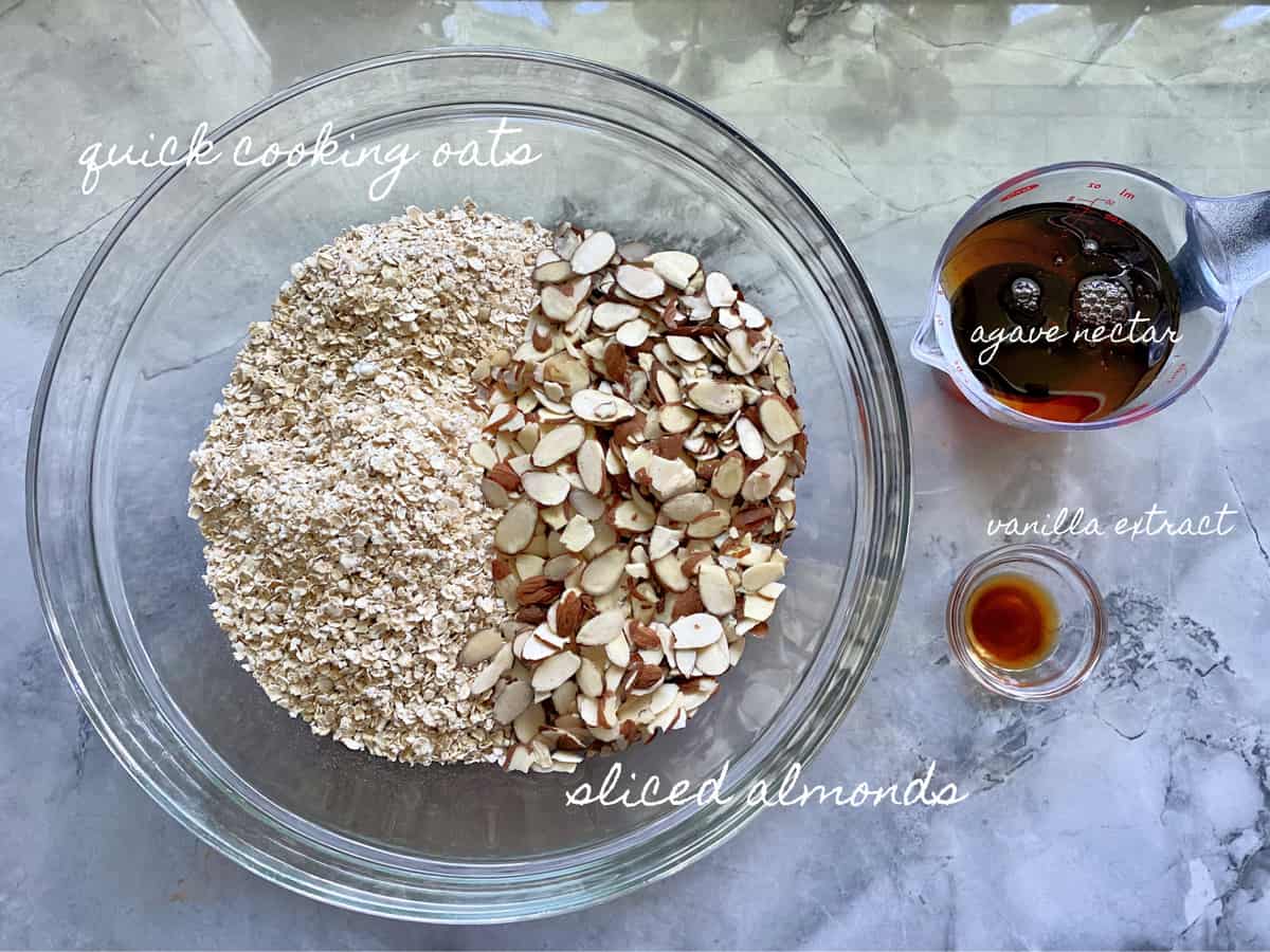 Ingredients on marble countertop; oats, sliced almonds, agave nectar, and vanilla extract.