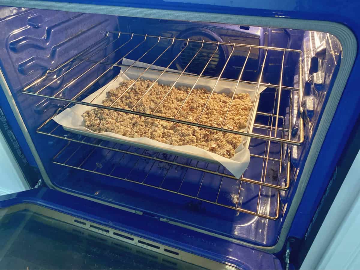 Granola on a parchment lined baking sheet inside a blue oven. 