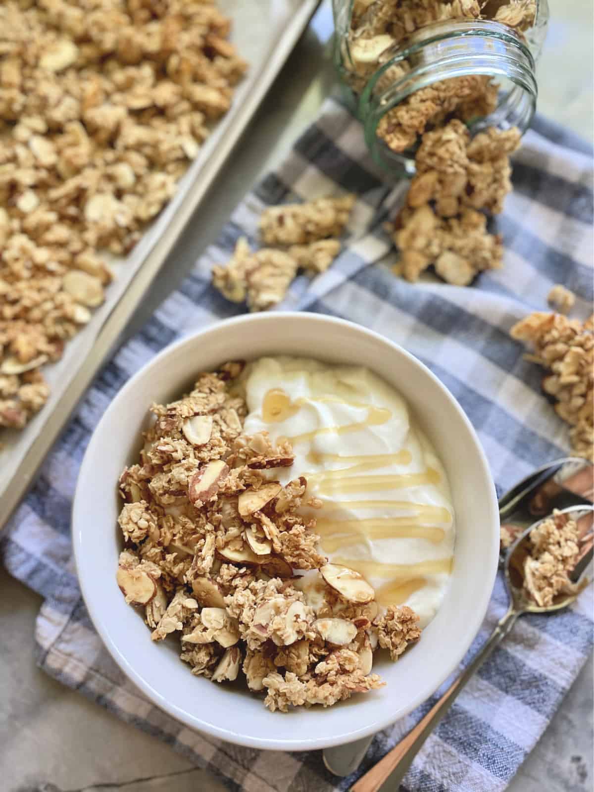 Top view of bowl of granola with yogurt, granola on tray and scattered around the bowl.