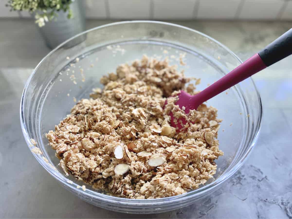 Top view of oats and almonds mixed together using a pink spatula in a glass bowl.
