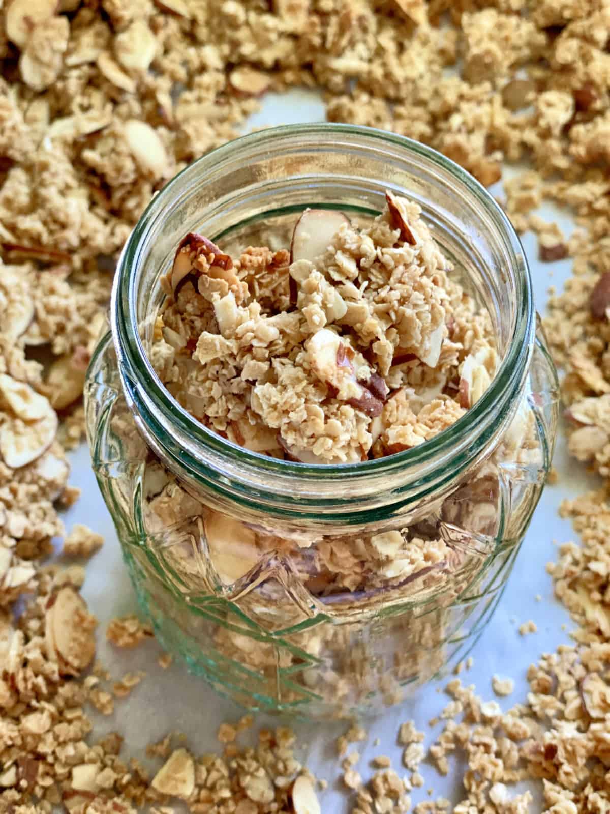 Glass mason jar filled with granola with almonds on a baking sheet of granola. 