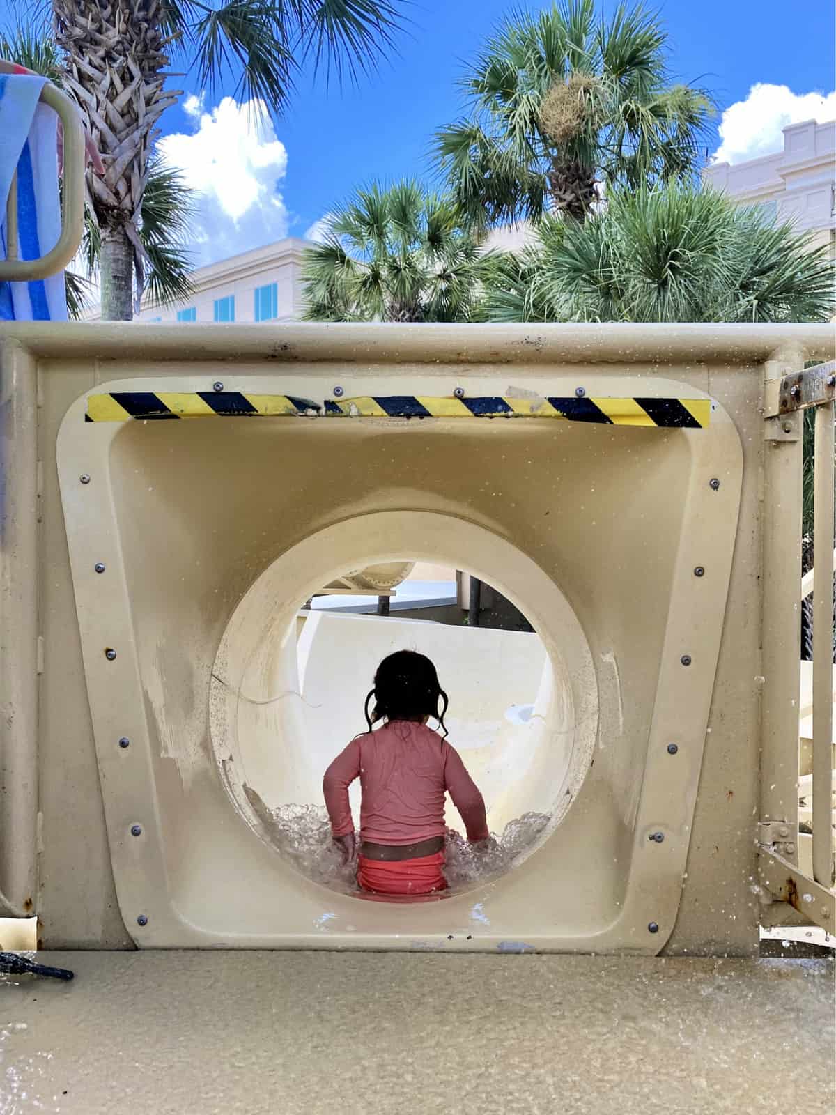 Back view of a little girl sliding down tan water slide.