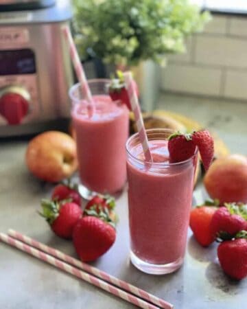 Two glasses filled with pink smoothie with strawberry on rim