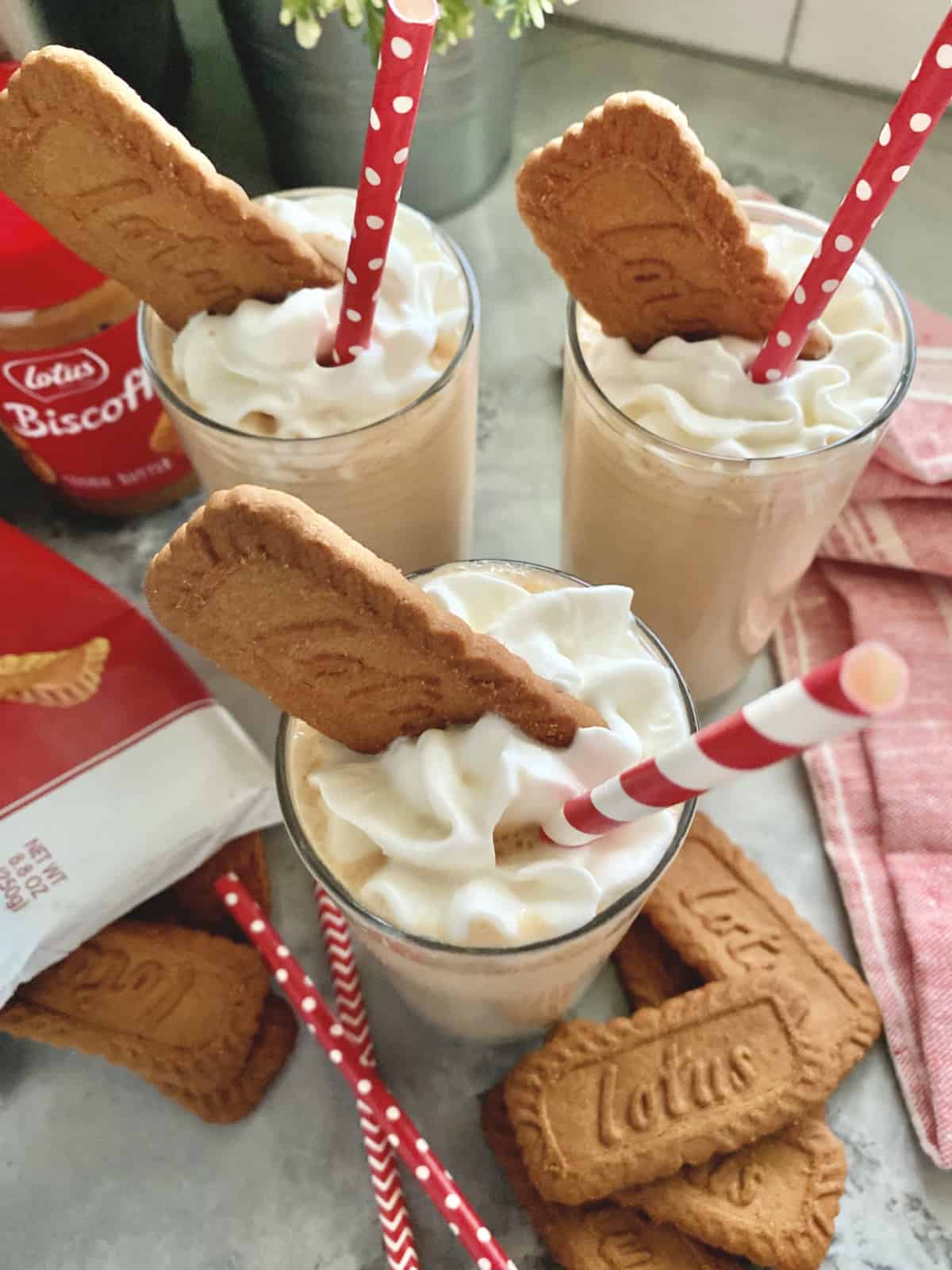 Top view of three milkshakes with red and white straws, whipped cream and a lotus cookie.